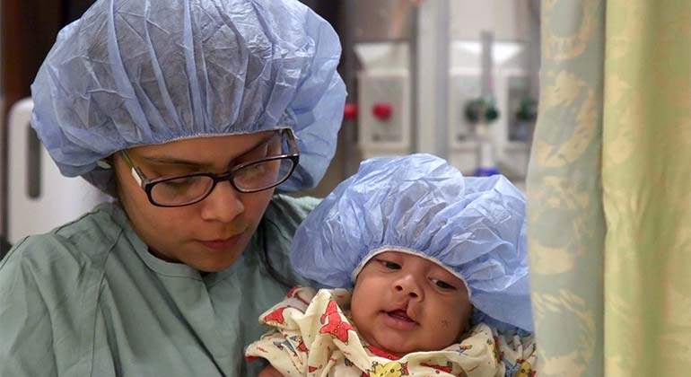 Male toddler about to undergo surgery for cleft lip palate reconstruction, sitting with mother at NYEE 